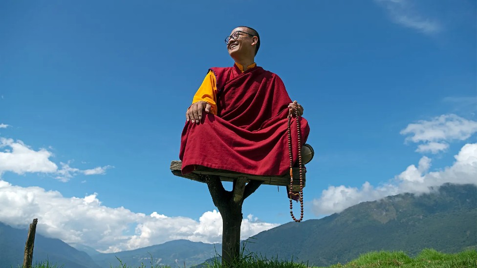 Rinpoche en un asiento elevado, detrás se aprecia el cielo