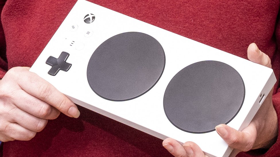 На этом крупном плане удерживаемого адаптивного контроллера Xbox показан белый прямоугольник, в котором преобладают две большие круглые кнопки - с дополнительными портами для дополнений сбоку