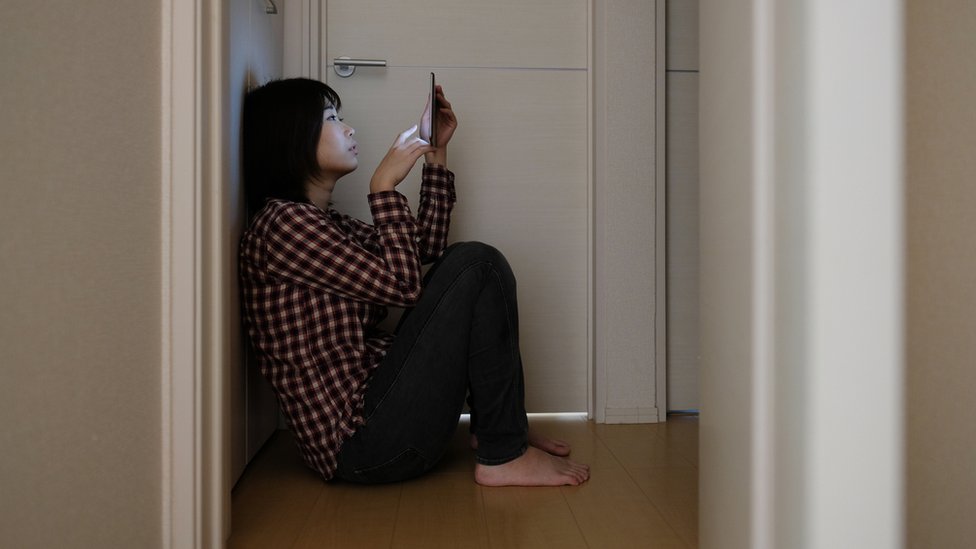 joven japonesa usando celular en un cuarto