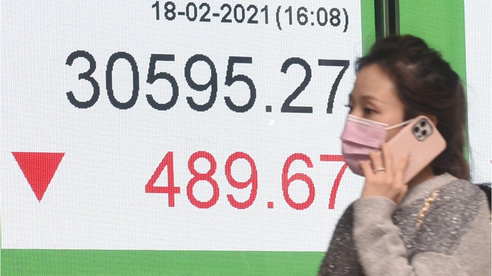 香港恆生銀行總行外一位女士走過股價報價屏幕（中新社照片18/2/2021）
