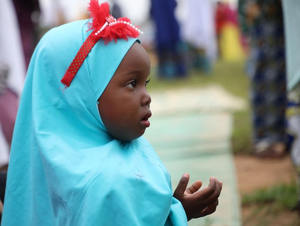 فتاة صغيرة ترتدي حجابا أزرق تؤدي الصلاة.