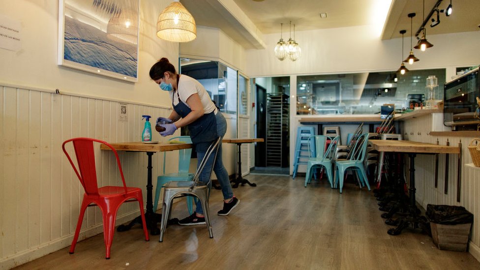 A mask waitress cleans a table