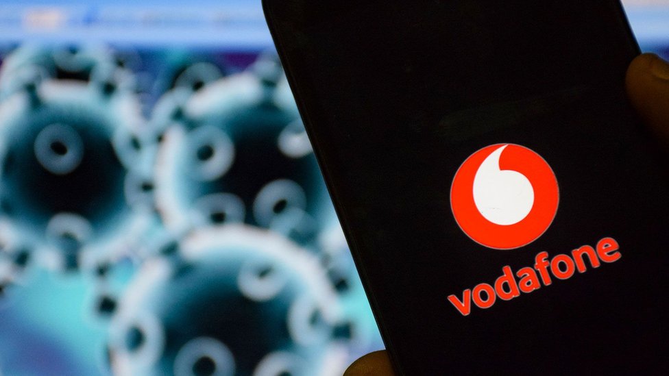 Виден мобильный телефон с логотипом Vodafone перед изображением коронавируса