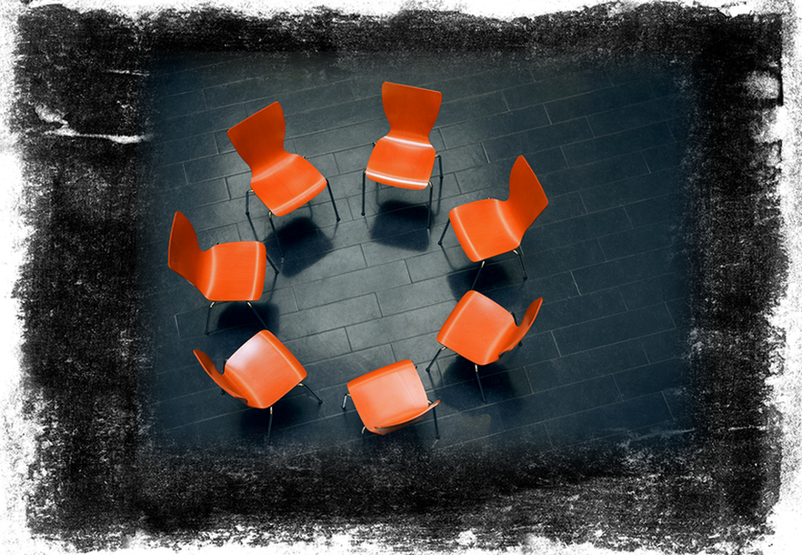 Stock image showing a circle of chairs facing each other on a black rustic background