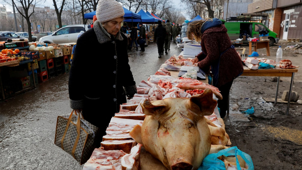 A woman looks at pig meat laid out at a market stall in occupied Mariupol