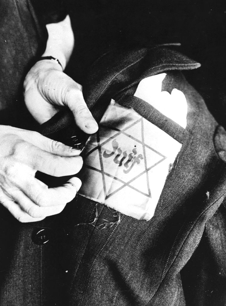 Unas manos cosen una estrella amarilla en una chaqueta que dice "judío".