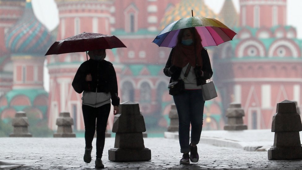 Люди ходят под зонтиками на Красной площади 29 мая 2020 года
