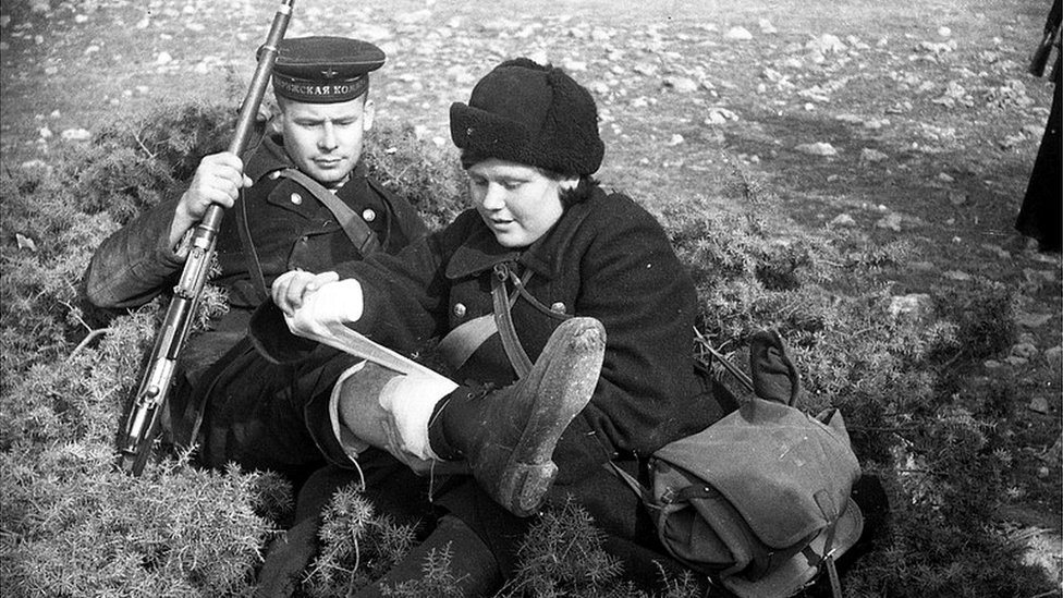Medsestra okazыvaet pomoщь ranenomu krasnoflotcu, na nogah kotorogo botinki, prislannыe po lend-lizu, 1942 g.