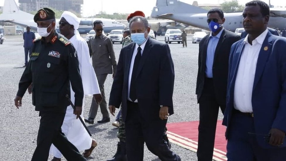 Премьер-министр Судана Абдалла Хамдок (C) носит маску в качестве превентивной меры против пандемии коронавируса (Covid-19), когда он присутствует на официальной церемонии похорон 59-летнего министра обороны Судана Гамаля Омера, скончавшегося в Джубе, столице страны. соседний Южный Судан, в международном аэропорту Хартума 25 марта 2020 года в Хартуме