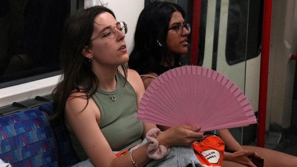 Metroda yelpazeyle serinlemeye çalışan bir kadın