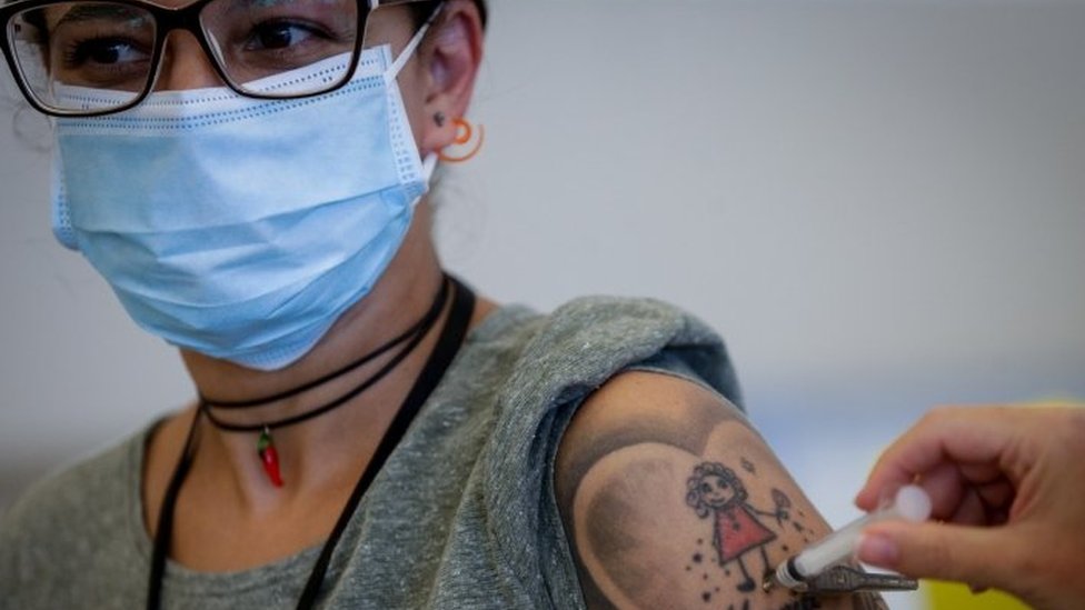 Mulher com braço tatuado e óculos recebe vacina