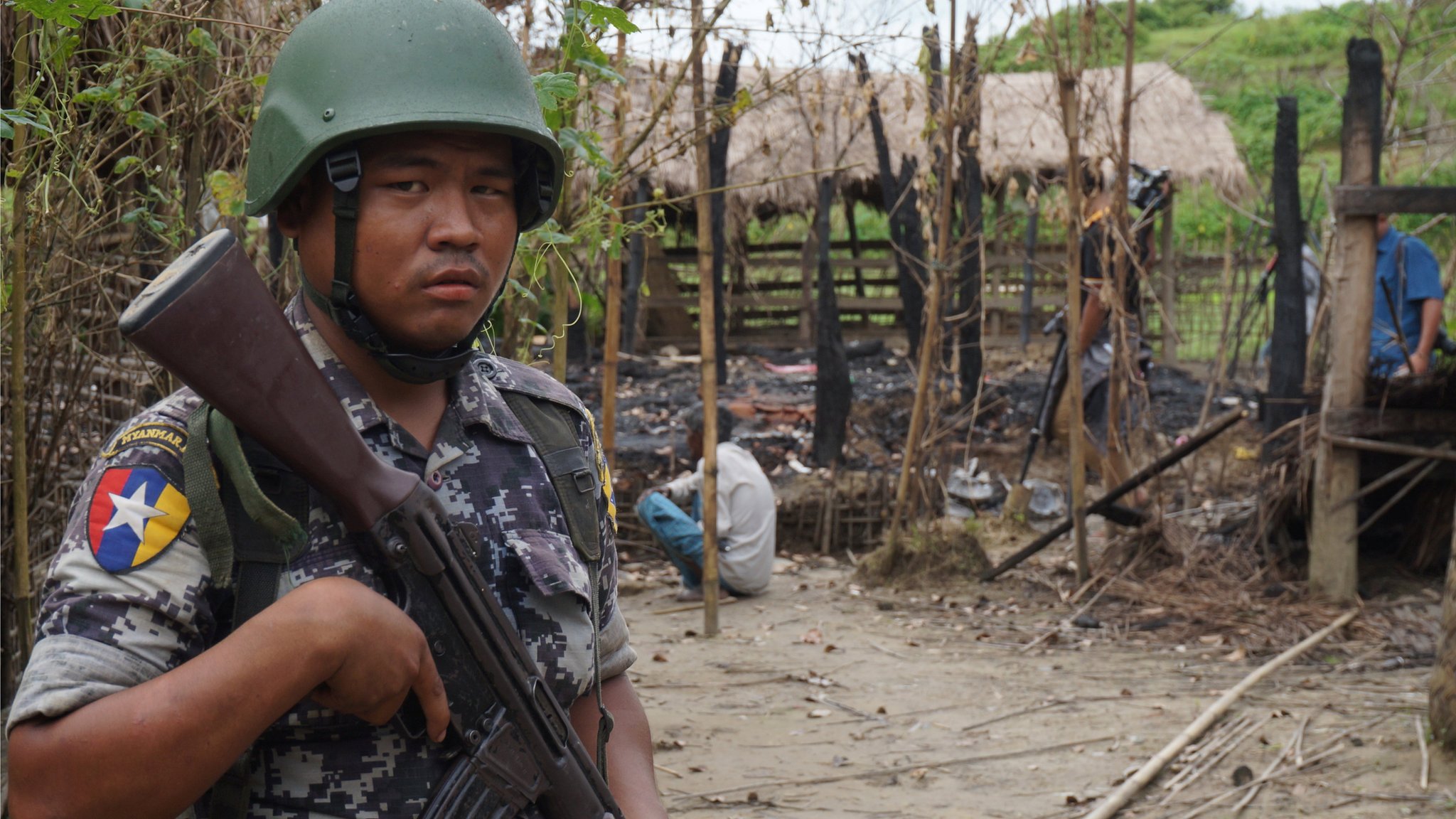 Офицер пограничной службы Мьянмы стоит на страже перед остатками дома, сгоревшего в результате столкновения между предполагаемыми боевиками и силами безопасности в деревне Тин Мэй, поселок Бутхидаунг, северный штат Ракхайн, Мьянма 14 июля 2017 г.