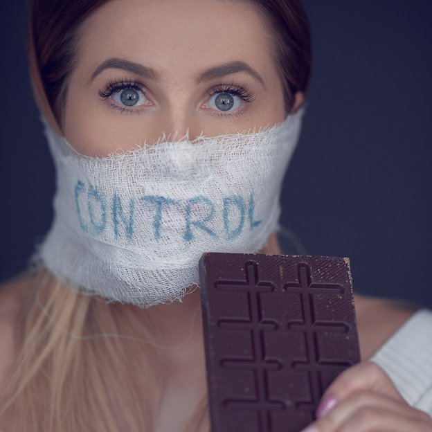 Mujer con tapabocas que dice "control" y un chocolate en la mano