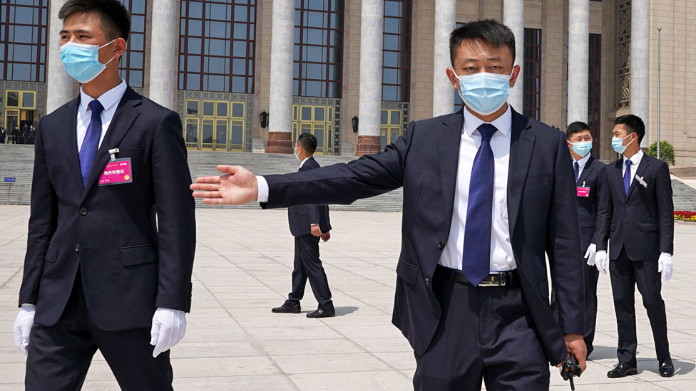 Security guards wearing face masks usher reporters outside of the Great Hall of the People at the end of the opening of the National People's Congress on 22 May 2020 in Beijing, China