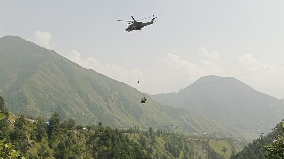 A soldier slings down from a helicopter above a cable car