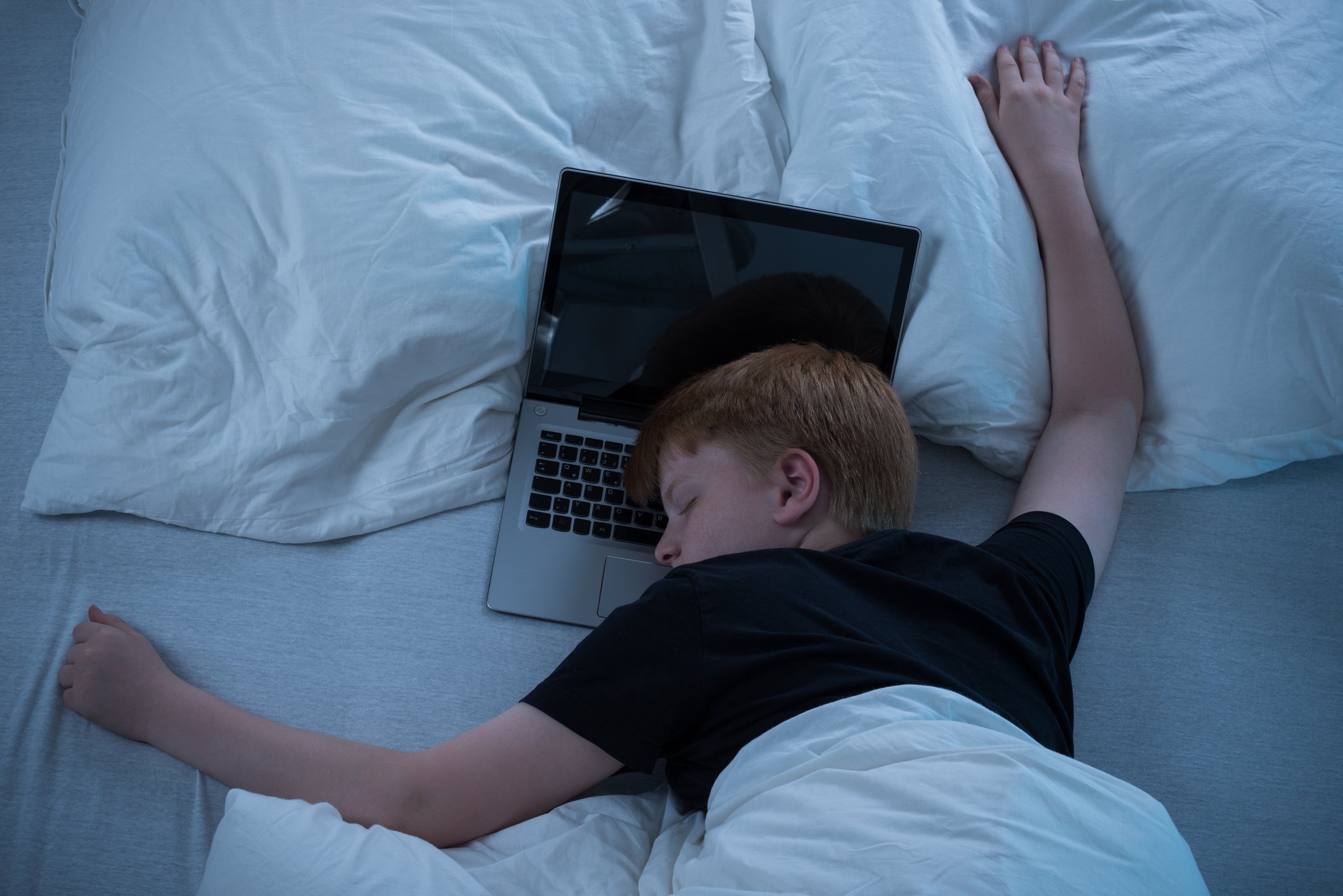 Niño pre-adolescente durmiendo en la cama con el ordenador.