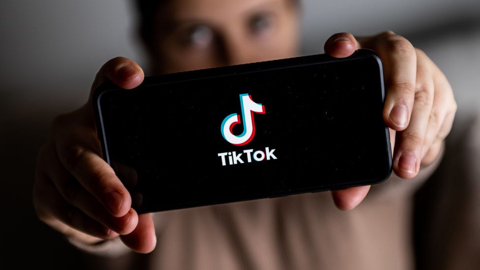 žena drži mobilni telefon na kome je logo društvene mreže Tiktok