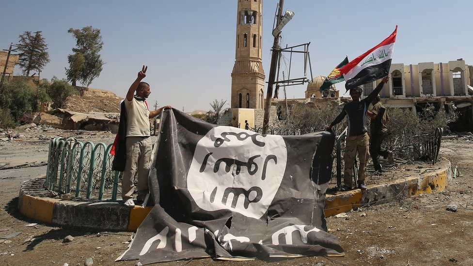 Бойцы «Хашед аш-Шааби» (отряды народной мобилизации), поддерживающие иракские силы, позируют с флагом группировки «Исламское государство» (ИГ) в Таль-Афаре 27 августа 2017 г.