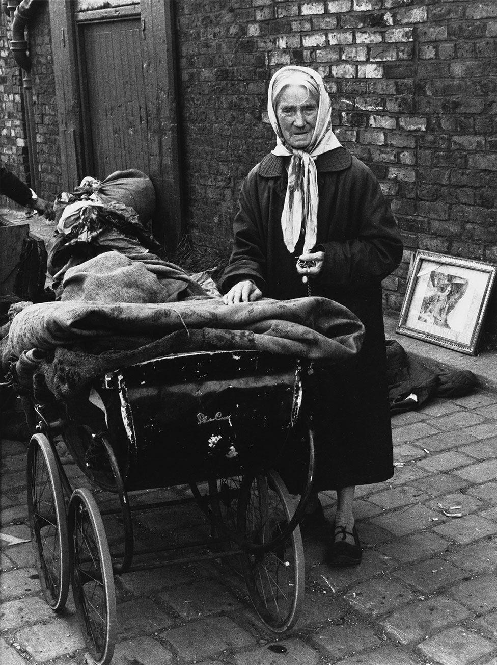 Пожилая женщина стоит рядом с коляской со связками ткани на