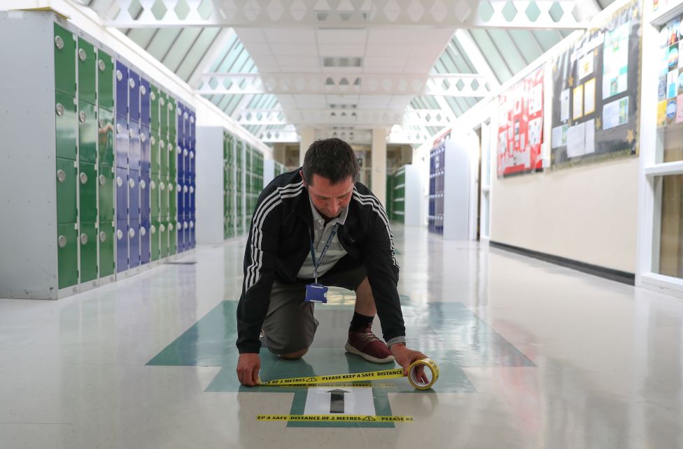 Лента социального дистанцирования прикреплена к одностороннему знаку в коридоре, поскольку идет подготовка к новому учебному семестру в школе Олдервуд в Олдершоте, Гэмпшир 26 августа 2020 г.