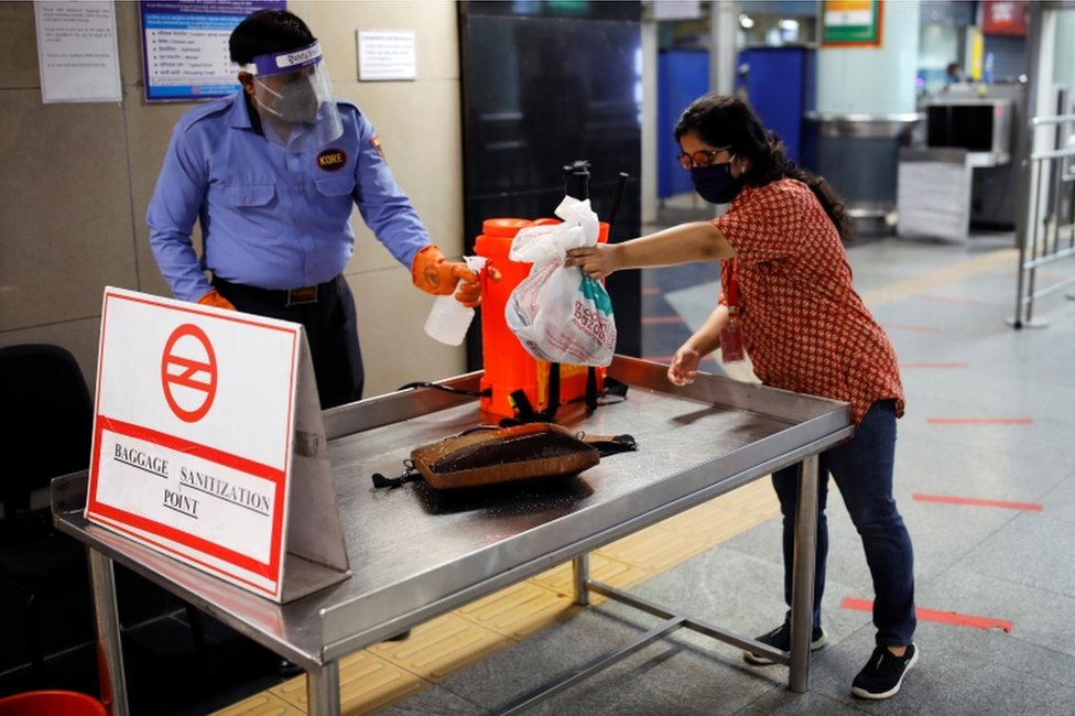 A security guard sprays disinfectant on a commuter"s bag at a Delhi metro train station, on the first day of the