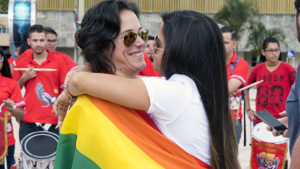 Una pareja de mujeres se abrazan envueltas en una bandera del orgullo gay fuera de la Corte Suprema en Costa Rica.