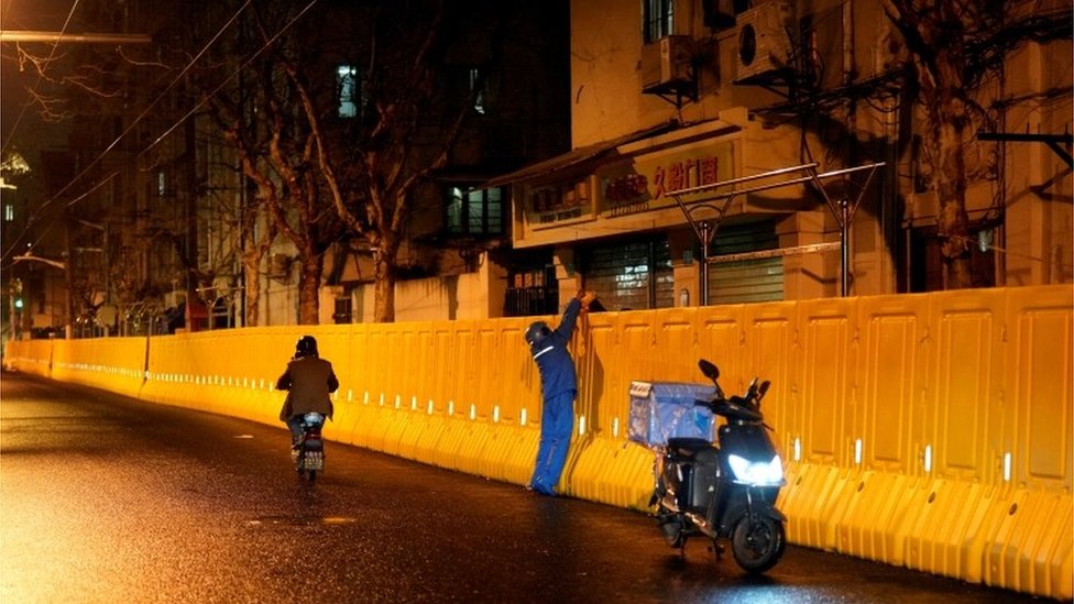 An Ele.me delivery worker hands a bag to a resident behind barriers sealing off an area, before the second stage of a two-stage lockdown to curb the spread of the coronavirus disease (COVID-19) in Shanghai, China, March 31, 2022.