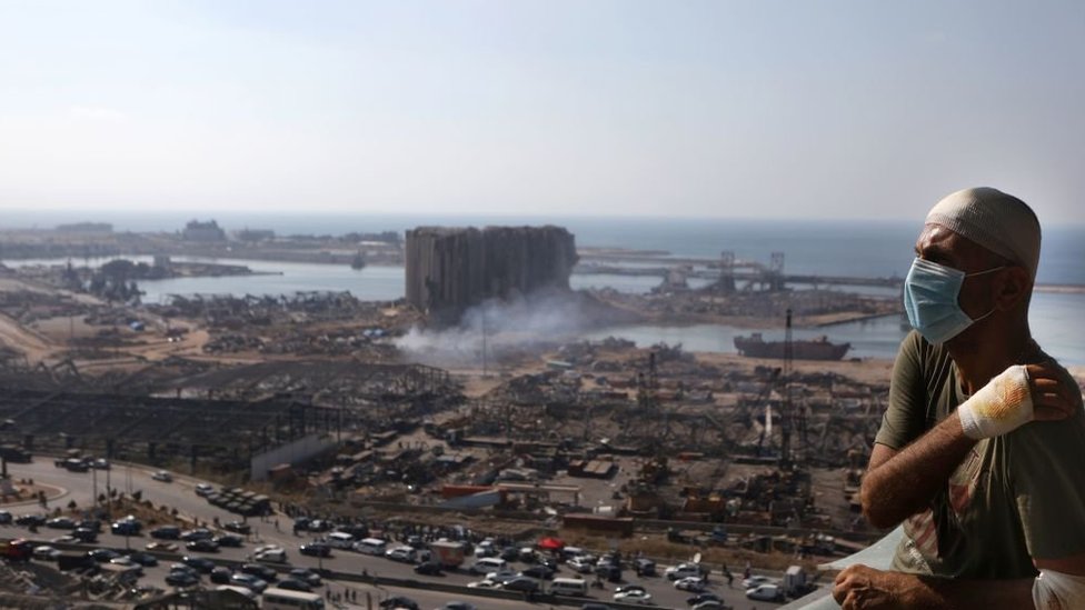شخص مصاب بانفجار بيروت، يظهر خلفه مرفأ بيروت