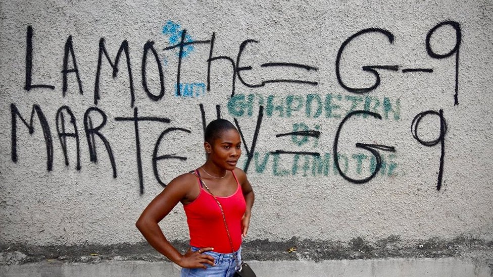 Una mujer frente a un graffiti de la banda G9.