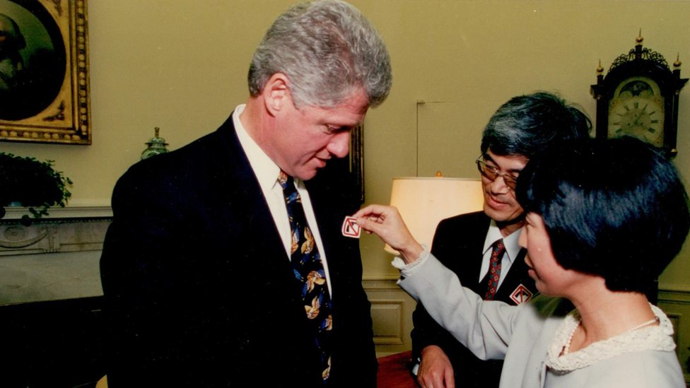 Mieko (centro) y Masa (derecha) poniéndole un adhesivo relacionado con el control de armas al entonces presidente Bill Clinton.