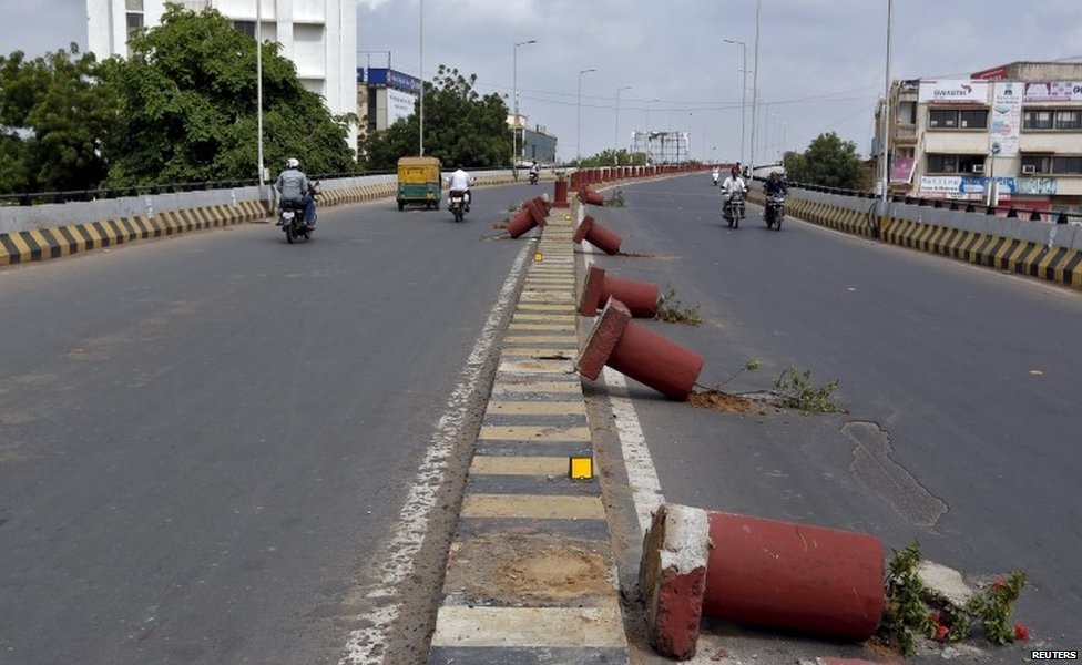 Транспортные средства проезжают мимо цветочных горшков, установленных на разделительной перегородке, которые были повреждены в ходе столкновений между полицией и протестующими в Ахмедабаде, Индия, 26 августа 2015 г.