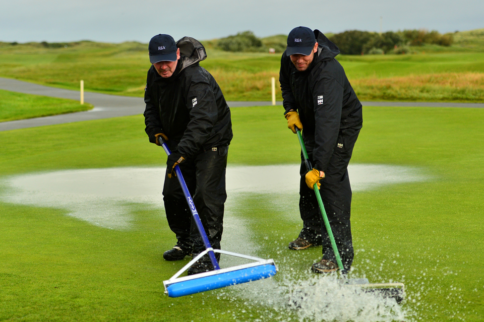 Two people sweep water from a golf green