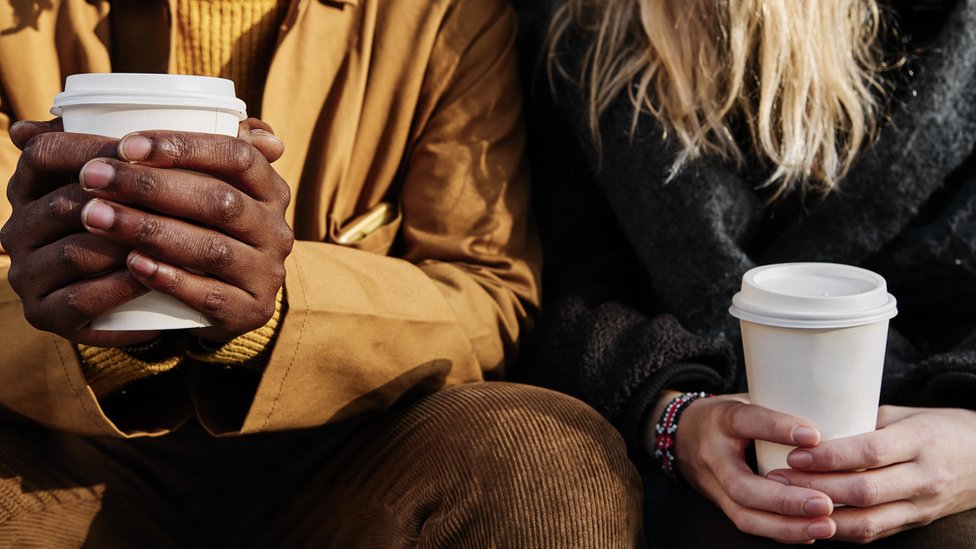 Dos personas sentadas sujetan vaso de café en las manos