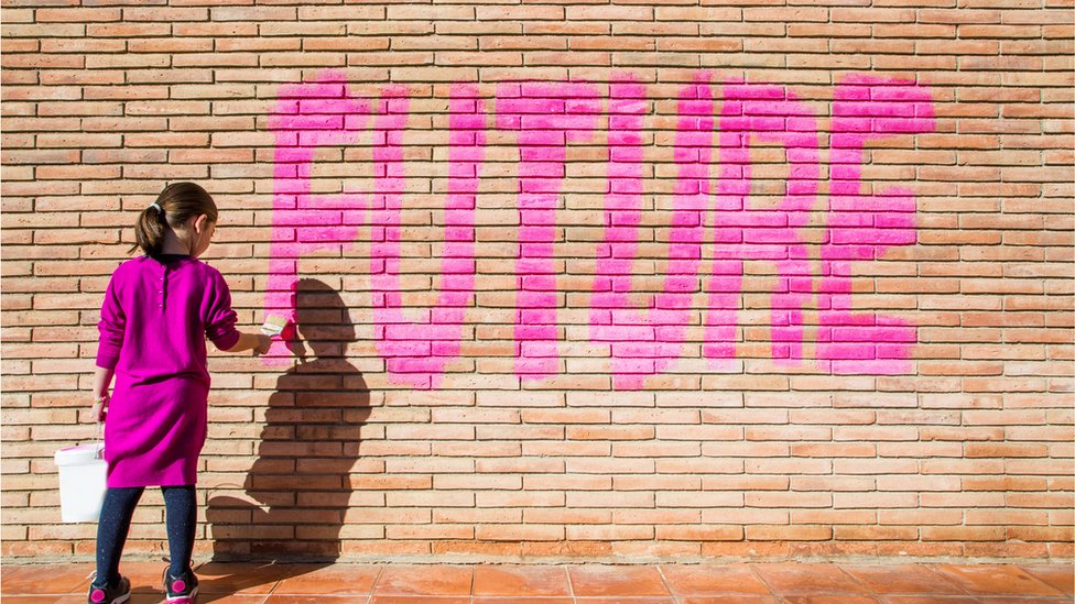 Una niña pinta la palabra Futuro en un muro de ladrillos