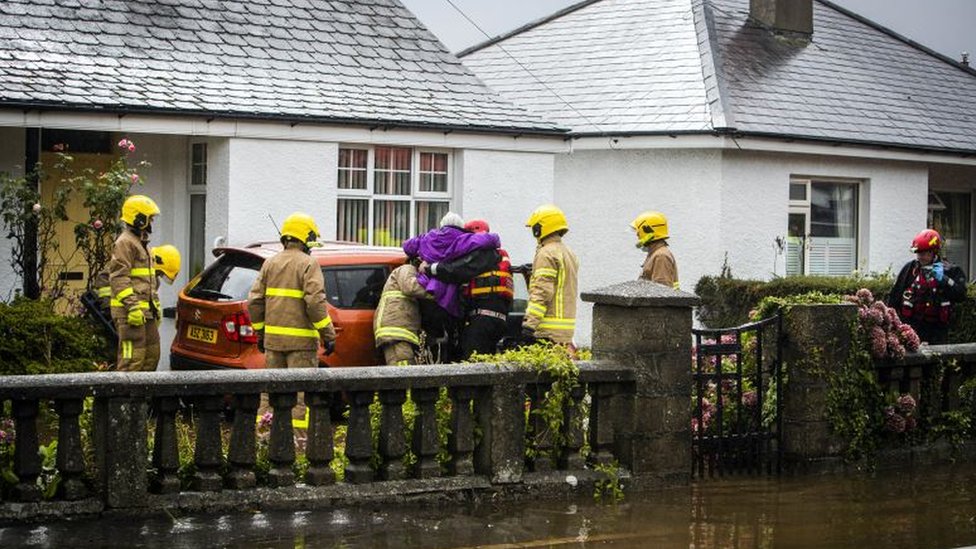 Группа пожарных помогает женщине выйти из дома