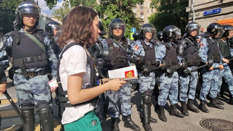 Olga walking in front of police with a copy of the Russian constitution