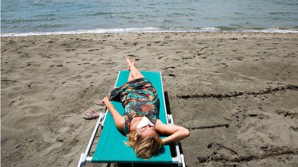 A woman wearing a face mask sunbathes at the beach after it officially reopened for the first time following the country"s strict coronavirus disease (COVID-19) lockdown, in Fregene, near Rome, Italy,