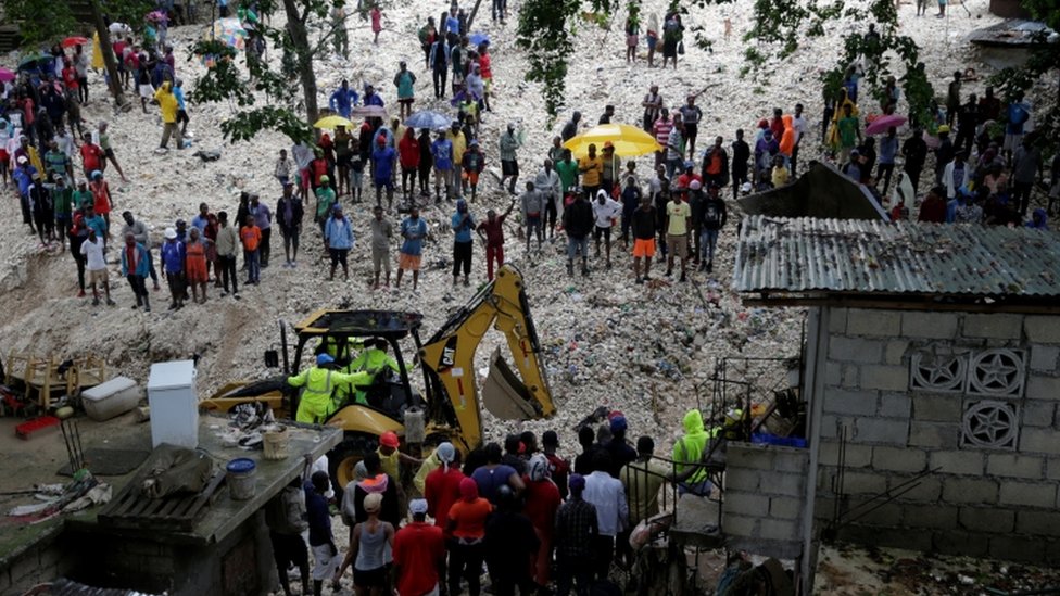 Жители смотрят на рабочих в районе, пострадавшем от прохождения тропического шторма Лаура, в Порт-о-Пренсе, Гаити