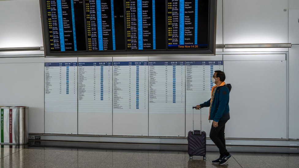 Un hombre con una maleta pasa frente a un tablero de información de vuelos en el Aeropuerto Internacional de Hong Kong.