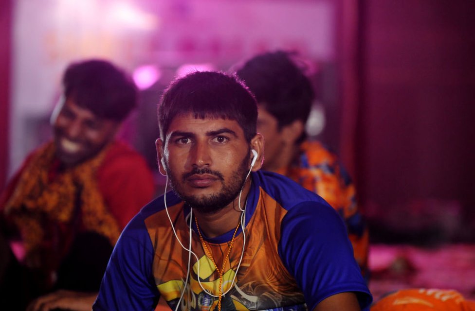 Канвария отдыхает, слушая музыку на своем телефоне, пока другие танцуют под религиозные песни в лагере в Дели 7 августа 2018 года.