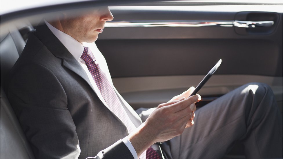 Hombre en traje leyendo en un dispositivo móvil y subiendo a un coche de lujo