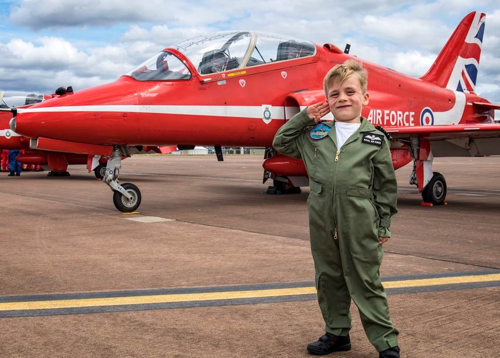 Мальчик салютует перед реактивным самолетом Red Arrow Hawk