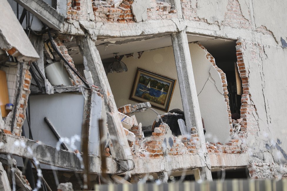 Поврежденное здание с дырой снаружи показывает картину, висящую на стене внутри, изображающую спокойную сцену катания на лодке