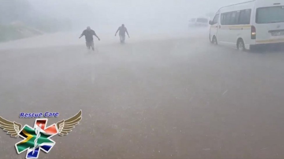 Люди пробираются через паводковые воды при сильном ветре и дожде рядом с затопленными автомобилями на дороге во время шторма в Дурбане, Южная Африка, 10 октября 2017 г.