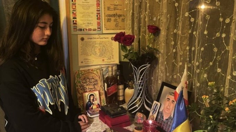 David Ratiani's daughter Mariam looks at a photo of her father on a table surrounded by Ukrainian and Georgian flags and roses.