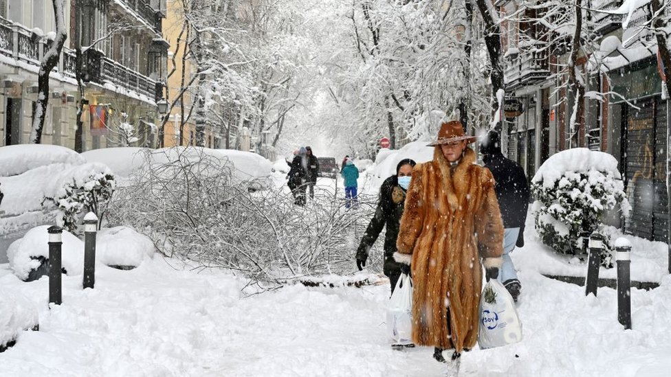 A woman wearing a fur coat walks amid a heavy snowfall in Madrid on January 9, 2021