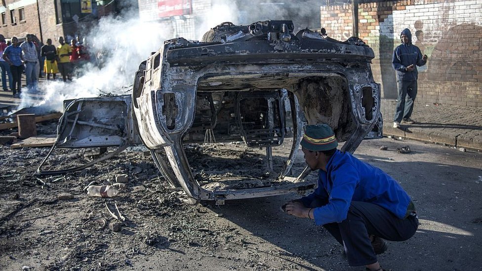 Люди смотрят на сгоревший автомобиль, подожженный рано утром возле Jeppies Hostles, в районе Jeppestown Йоханнесбурга, 17 апреля 2015 г.