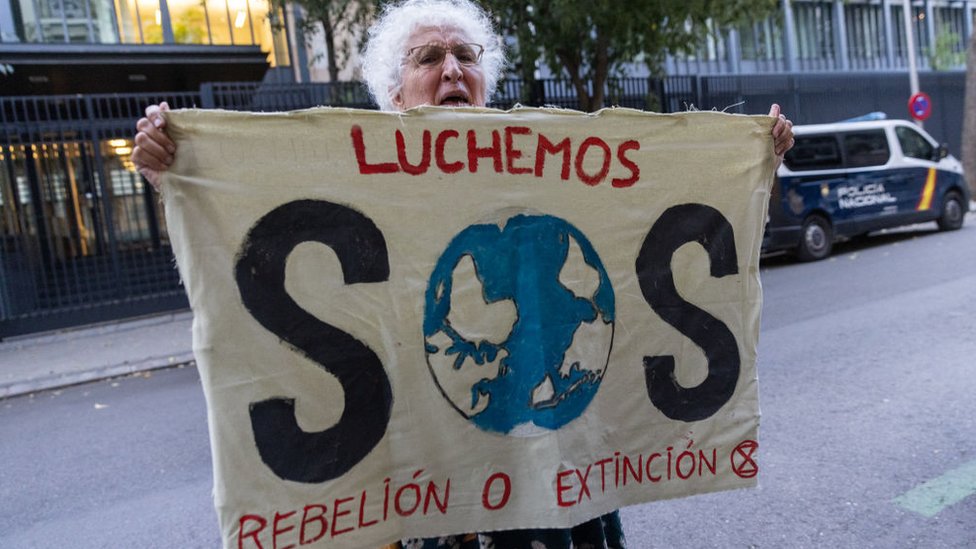 Una mujer sostiene una bandera con la leyenda: Luchemos. SOS. Rebelión o extinción