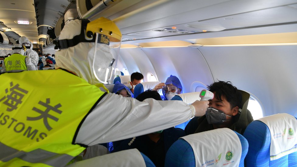 Funcionário da imigração realiza verificação de temperatura a bordo depois que um voo pousou na China