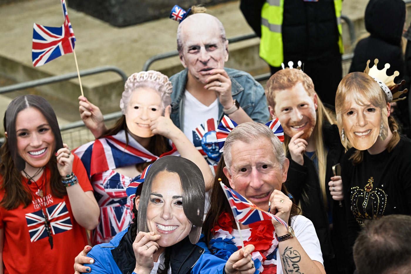 Well-wishers wearing masks of members of the Royal Family wait along the route of the procession